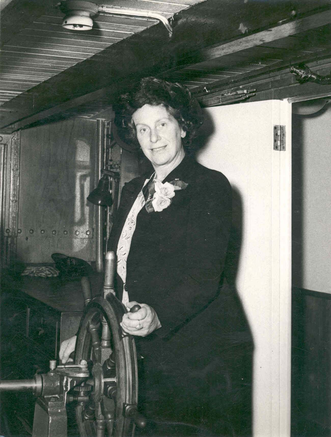 Dame Caroline Haslett, standing at ships wheel