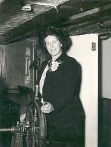Dame Caroline Haslett, standing at ships wheel